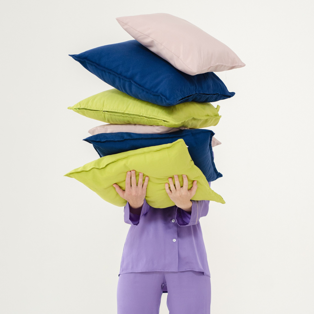 A woman in purple pajamas holds a stack of colorful pillows.